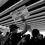 White male marching with protestors, holding sign that reads "with privilege comes responsibility"