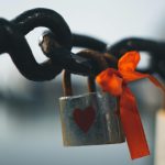 Close-up of a heart-shaped love padlock with a red ribbon on a metal chain in Liverpool